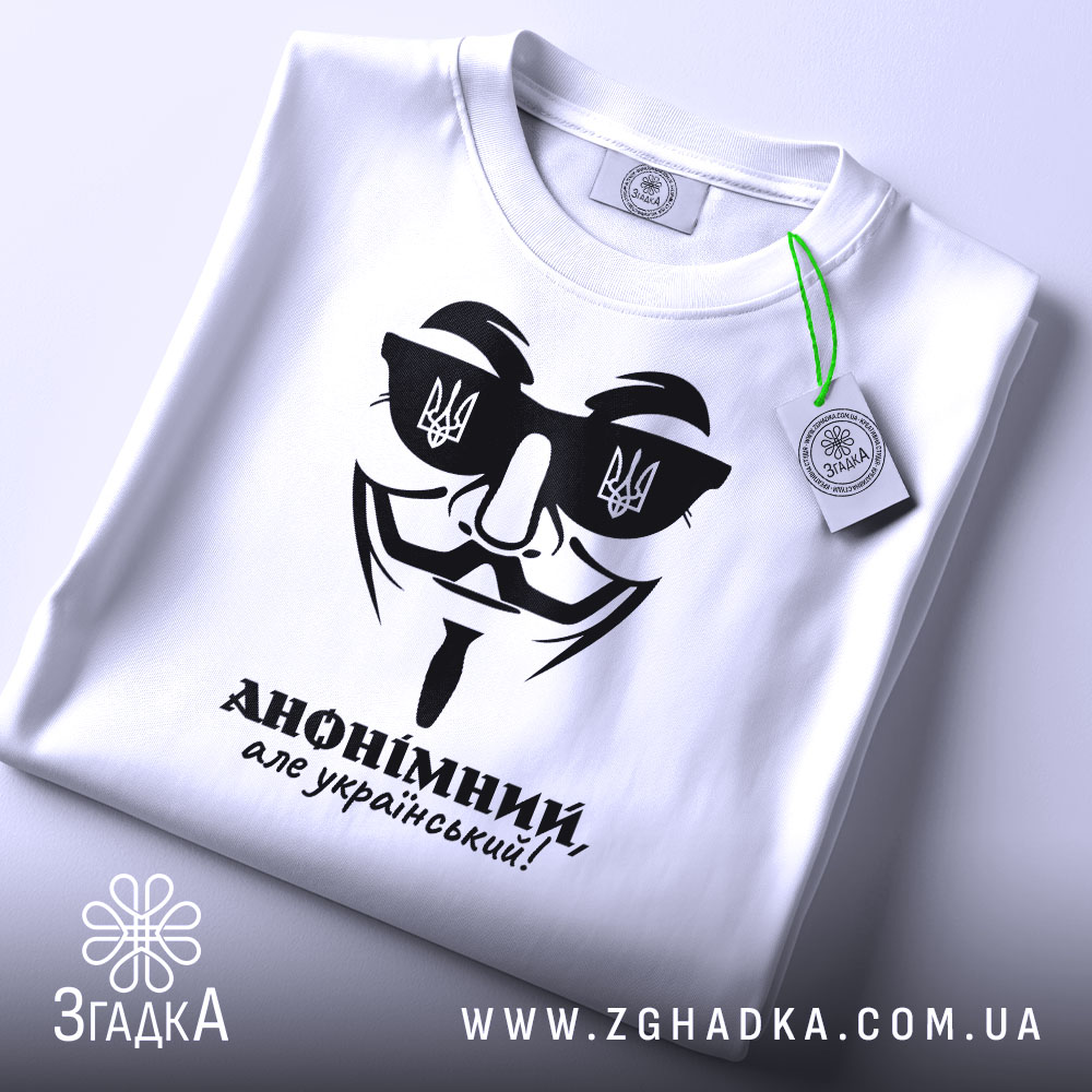 Футболка анонімний український, біла, складена на плоскій поверхні, фон світлий, принт чорного кольору з зображенням маски та написом 'АНОНІМНИЙ, але український!', на комірці видно етикетку.