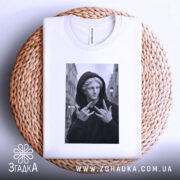 Футболка античний стріт, біла, складена на плетеній основі, фон світло-сірий, принт з чорно-білим зображенням статуї в капюшоні, яка показує жест.