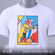Футболка арт герої білого кольору, зображена зверху на плоскій поверхні, фон світло-сірий. Принт яскравий, з кольоровими персонажами, що посміхаються, з елементами жовтого, червоного та блакитного кольорів, з прикріпленою етикеткою.