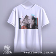 Футболка арт кохання, біла, підвішена на вішалці, фон світло-сірий, принт з двома людьми, що цілуються, з елементами графіки, вид з переду.