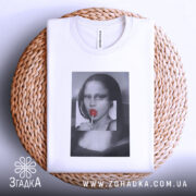 Футболка арт лоліпоп, біла, складена на плетеній кошику, фон світло-сірий, принт з жінкою з червоним льодяником, видна етикетка на комірці.