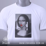 Футболка арт лоліпоп, біла, складена на поверхні, фон світло-сірий, принт з жінкою з червоним льодяником, на комірці видна етикетка.