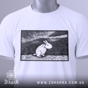 Футболка арт заєць білого кольору, складена на поверхні, ракурс зверху, фон світло-сірий, принт з зображенням зайця в стилі лінійного малюнка, прикріплена етикетка з зеленим шнурком.