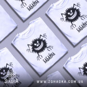 Футболка бабайка білого кольору, зображена з близького ракурсу на манекені, фон світло-сірий, принт чорного кольору з веселим персонажем та написом 'БАБАЙКА'.