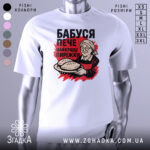 Футболка бабуся пече пиріжки, біла, зображена на манекені, фон світло-сірий, принт з бабусею, що тримає пиріжки, червоний фон за принтом.