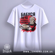 Футболка бабуся пече пиріжки, біла, зображена на вішалці, фон світло-сірий, принт з бабусею, що тримає пиріжки, червоний фон за принтом.