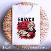Футболка бабуся пече пиріжки, біла, зображена зверху на плетеному кошику, фон світло-сірий, принт з бабусею, що тримає пиріжки, червоний фон за принтом.