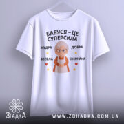 Футболка бабуся це суперсила, біла футболка, підвішена на вішалці, на фоні світло-сірого кольору, принт з бабусею та текстом 'Бабуся – це суперсила', оточений зірочками та сердечками.