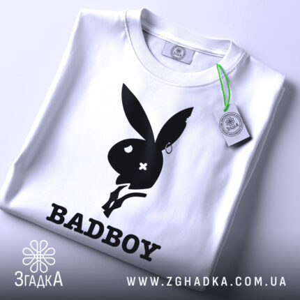 Футболка badboy кролик білого кольору, зображена зверху, на ній видно етикетку з зеленим шнурком, фон світло-сірий, принт чорного кольору з силуетом кролика та написом 'BADBOY'.