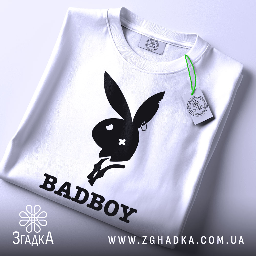 Футболка badboy кролик білого кольору, зображена зверху, на ній видно етикетку з зеленим шнурком, фон світло-сірий, принт чорного кольору з силуетом кролика та написом 'BADBOY'.