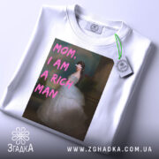 Футболка багата незалежна, білого кольору, зображена зверху, фон світлий, принт з написом 'MOM, I AM A RICH MAN' у рожевих літерах на фоні зображення жінки в білій сукні, на комірці є етикетка.