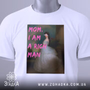 Футболка багата незалежна, білого кольору, зображена зверху, фон світлий, принт з написом 'MOM, I AM A RICH MAN' у рожевих літерах на фоні зображення жінки в білій сукні, на комірці є етикетка.