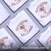 Футболка Ballerina Cappuccino білого кольору, зображена з правого ракурсу, на манекені. Принт з малюнком балерини, що танцює, з чашкою капучино замість голови, оточено сердечками. Фон світло-сірий.