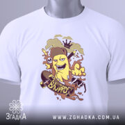 Футболка банан скейтер білого кольору, зображена зверху, на столі, фон світло-сірий, принт з жовтим бананом у шапці, що катається на скейтборді, з веселими елементами, на футболці є етикетка з зеленим шнурком.