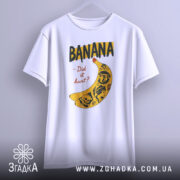 Футболка банан тату білого кольору, підвішена на вішалці, ракурс спереду, фон світло-сірий, принт з жовтою бананою та чорними написами, деталі принта включають малюнки черепів та інших елементів.