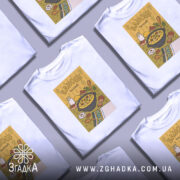 Футболка банош українська кухня, біла, зображена на манекені, фон світло-сірий, принт з жовтим фоном, на якому зображена каструля з баношем, молоко, хліб та інші інгредієнти.