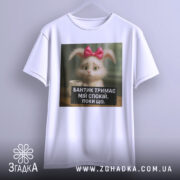 Футболка бантик тримає спокій, біла, підвішена на вішалці, фон світло-сірий, принт з кроликом з рожевим бантиком і текстом на чорному фоні.