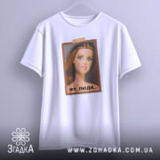 Футболка барбі фу люди. Біла футболка, підвішена на вішалці, з принтом ляльки, що має вираз обличчя, який демонструє незадоволення. Принт оформлений у рамці коричневого кольору, фон світло-сірий. Футболка має короткі рукави.