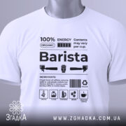 Футболка бариста стиль, біла, складена на столі, фон світло-сірий, принт чорного кольору з текстом та іконками, на футболці є етикетка з зеленим шнурком.
