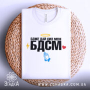 Футболка БДСМ білого кольору, зображена на плетеній основі, фон світло-сірий, принт містить текст "Боже дай сил мені БДСМ" з жовтим німбом, блискавкою, блакитними руками та червоним сердечком.