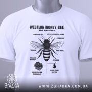 Футболка бджола принт білого кольору, складена на поверхні, фон світло-сірий, принт чорного кольору з зображенням бджоли та текстом, на футболці зелений ярлик.
