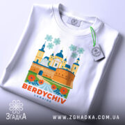 Футболка Бердичів, біла, зображена зверху, фон світло-сірий, принт з архітектурними елементами та квітами, текст 'BERDYCHIV UKRAINE' яскраво-оранжевий, на комірці видна етикетка.