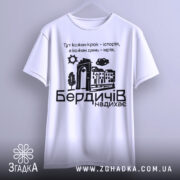 Футболка Бердичів надихає. Біла футболка з коротким рукавом, підвішена на вішалці, фон світло-сірий. Принт на футболці містить текст і графічні елементи, що зображують місто.