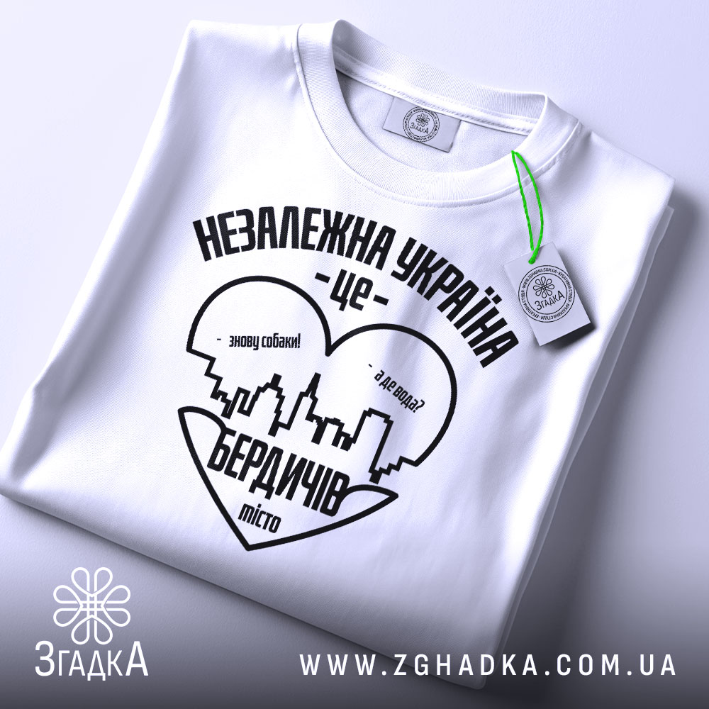 Футболка Бердичів подарунок, біла, складена на поверхні, фон світло-сірий, принт чорного кольору з написом 'Незалежна Україна - це Бердичів' та силуетом міста, з зеленим ярликом.