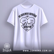 Футболка Бердичів подарунок, біла, підвішена на вішалці, фон світло-сірий, принт чорного кольору з написом 'Незалежна Україна - це Бердичів' та силуетом міста.