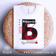 Футболка Бердичів заснований, біла, складена на плетеній кошику, фон світлий, принт містить червоний та чорний текст з графічними елементами.