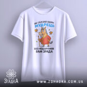 Футболка без подарунків зрада. Білий колір, зображена спереду на манекені, фон світло-сірий. Принт з мультяшним конем у червоному халаті, що тримає палицю, з пташками навколо.