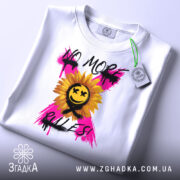 Футболка без правил, біла, складена на поверхні, фон світлий, принт з соняшником, усміхненим обличчям та написом 'NO MORE RULES!' у яскравих кольорах, з етикеткою на комірці.