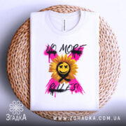 Футболка без правил, біла, складена на плетеній кошику, фон світлий, принт з соняшником, усміхненим обличчям та написом 'NO MORE RULES!' у яскравих кольорах.