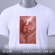 Футболка білка лісова марка, біла, зображена на столі, фон світлий, принт з білкою на дереві в червонувато-коричневих тонах, з етикеткою зеленого кольору.