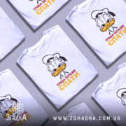 Футболка більше спати, біла, зображена з фронтального ракурсу на манекені, фон нейтральний, принт з мультяшним персонажем, що має сонний вираз обличчя, текст "ТРЕБА БІЛЬШЕ СПАТИ" червоного і жовтого кольорів.