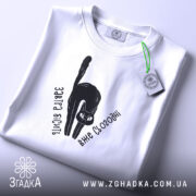 Футболка бісить вже сьогодні, складена біла футболка з чорним принтом кота, текстом 'Завтра бісить вже сьогодні', на фоні світло-сірого кольору, з зеленим ярликом.