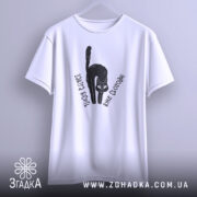 Футболка бісить вже сьогодні, біла футболка, підвішена на вішалці, з чорним принтом кота, текстом 'Завтра бісить вже сьогодні', фон світло-сірий.