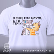 Футболка бісити терпіти, біла, складена на поверхні, фон світлий, принт з двома котами, один з котів з жовтими смужками, інший сірий, текст українською: 'Я буду тебе бісити, а ти терпи!', з етикеткою зеленого кольору.