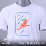 Футболка біжу волосся позаду, біла, складена на поверхні, фон світлий, принт з рожевим персонажем, що біжить, з короною та блакитним волоссям, прикріплена етикетка з логотипом.