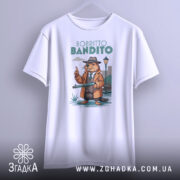 Футболка Bobritto Bandito білого кольору, підвішена на вішалці, фон світло-сірий, принт з ведмедем у капелюсі та пальто, що тримає гвинтівку, на фоні вуличного ліхтаря.