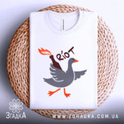 Футболка бойовий гусак, біла, зображена зверху, на фоні плетеного кошика, принт з гусаком, що тримає пляшку з вогнем, виконаний у сірому, оранжевому та чорному кольорах.