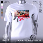 Футболка Bombardiro Crocodilo білого кольору, зображена на манекені з правого боку, фон нейтральний, принт з крокодилом, що тримає бомби, на фоні міського пейзажу.