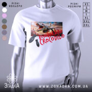 Футболка Bombardiro Crocodilo білого кольору, зображена на манекені з правого боку, фон нейтральний, принт з крокодилом, що тримає бомби, на фоні міського пейзажу.