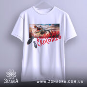 Футболка Bombardiro Crocodilo білого кольору, зображена на манекені з фронтального ракурсу, фон світло-сірий, принт з крокодилом та бомбами, кольори яскраві.