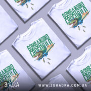 Футболка Bombardiro Crocodilo білого кольору, зображена на манекені з правого боку, фон світло-сірий, принт з крокодилом в пілотських окулярах, що сидить в літаку, з зеленим текстом 'BOMBARDIRO CROCODILO' та деталями бомб, що падають.