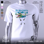 Футболка Бомбардіро Крокоділо білого кольору, зображена з фронтального ракурсу на манекені, фон нейтральний, принт з крокодилом, що літає на літаку, з бомбами під ним.
