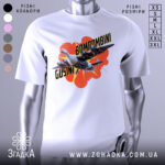 Футболка Bombombini Gusini білого кольору, зображена на манекені, з принтом, що містить птаха та літаки на яскравому фоні з червоними елементами.