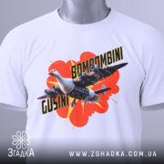 Футболка Bombombini Gusini білого кольору, складена на поверхні, з принтом птаха та літаків, на фоні червоного вибуху, з етикеткою, що звисає.