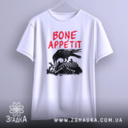 Футболка Bone Appétit білого кольору, підвішена на вішалці, ракурс спереду, фон світло-сірий, принт з чорним вороном, що клює кістки, текст червоним шрифтом 'BONE APPÉTIT'.