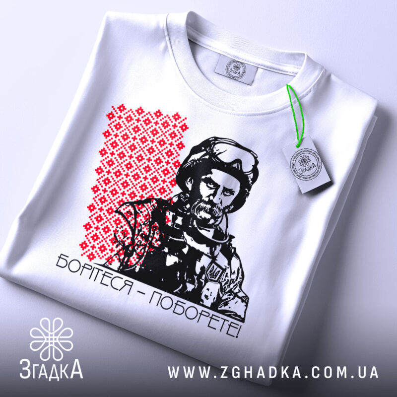 Футболка борітеся поборете, білого кольору, зображена в верхньому ракурсі, фон світло-сірий, принт з червоним орнаментом та чорно-білим зображенням чоловіка в військовій формі, на футболці є етикетка з зеленим шнурком.